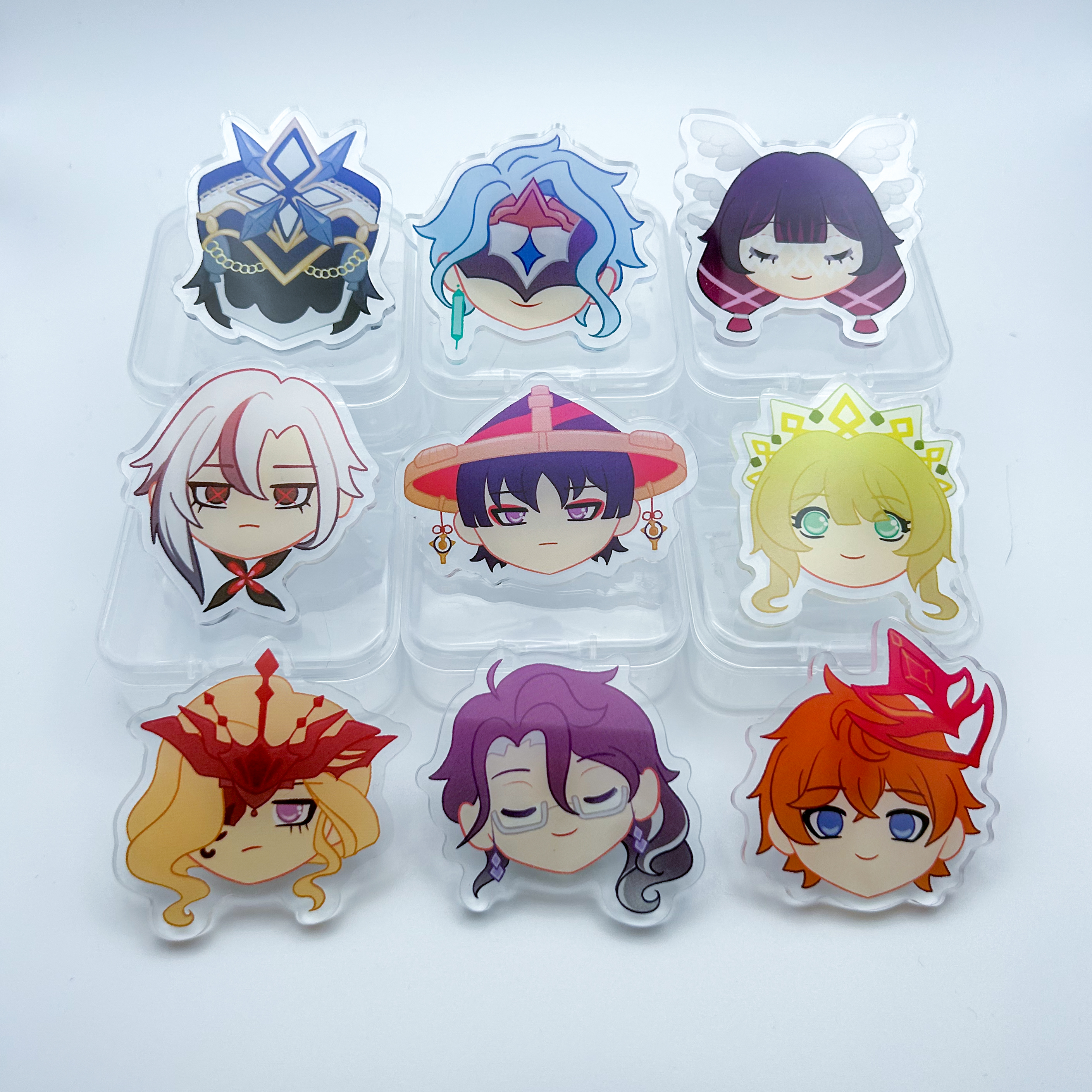 Harbinger Head Acrylic Pins - 9 clear acrylic pins, each depicting the head of a Fatui Harbinger from Genshin Impact. Featured are the following: Capitano, Dottore, Columbina, Arlecchino, Scaramouche, Sandrone, Signora, Pantalone, and Childe.